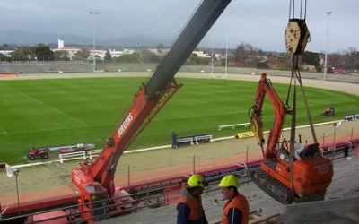 Crane lifting a mini excavator into the Arena Manawatu grandstand above the sports field