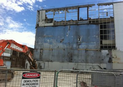 Jurgens excavator stripping cladding from the Fonterra Longburn powder factory behind a "Demolition in progress" sign