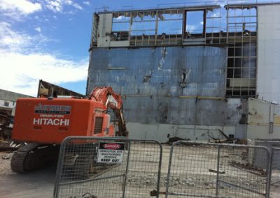 Hitachi excavator in Jurgens livery beside the stripped steel frame of the Fonterra Longburn powder factory