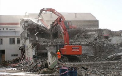Hitachi excavator demolishing the Makarewa freezing works building with an operator directing from the ground