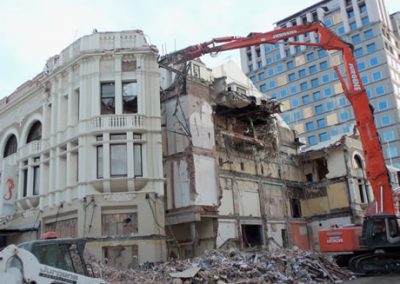 High reach excavator removing the upper floors of the Regent Buildings beside a modern glass tower