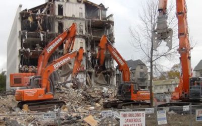 Two Jurgens excavators demolishing the earthquake-damaged Scales House beside a sign reading "This building is dangerous and not safe to enter"