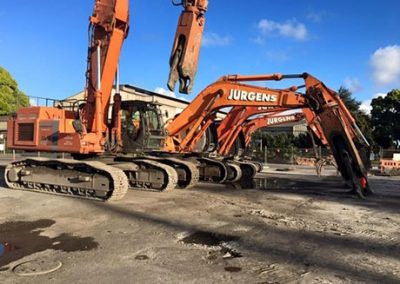Three orange Jurgens demolition excavators with shear and grapple attachments parked in the yard
