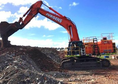 Jurgens excavator working on a large pile of demolition rubble under a blue sky