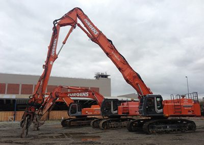 Two Jurgens high reach demolition excavators with long booms parked beside an industrial building