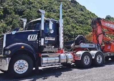 Jurgens Mack truck with a low-loader trailer carrying an excavator on a coastal road