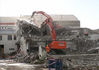 Hitachi excavator with a demolition attachment tearing into a large industrial building