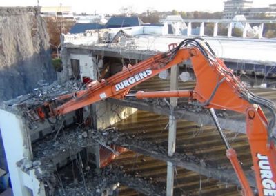 Jurgens excavator arm reaching across the exposed upper floors of Scales House, with Christchurch rooftops behind