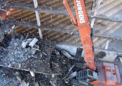 Overhead view of a Jurgens excavator boom working among rubble and exposed reinforcing steel inside Scales House