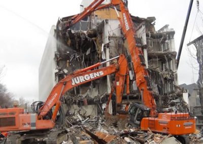 Two Jurgens excavators working on the stripped concrete frame of Scales House
